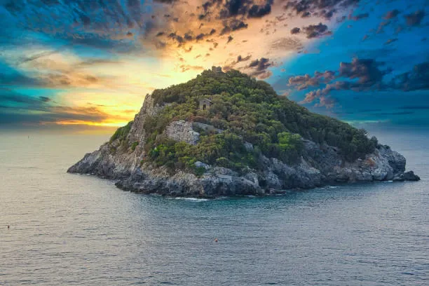 Alba sul mare con l'isola in controluce e la costa rocciosa in primo piano
