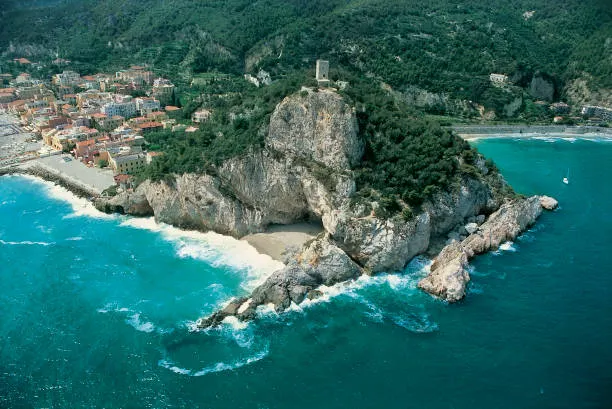 Promontorio roccioso che entra nel mare turchese, con la torre in cima e il paese sullo sfondo
