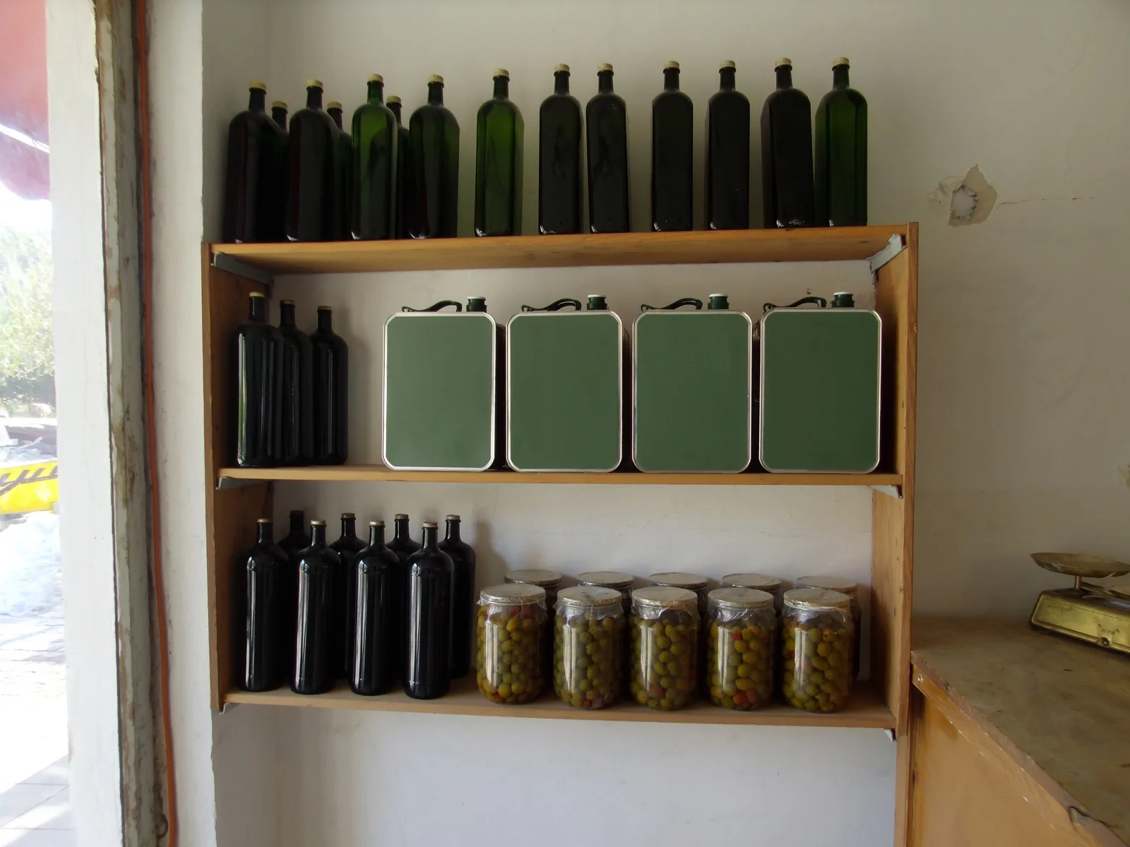 Lo scaffale della bottega con bottiglie, latte e vasi di olive.