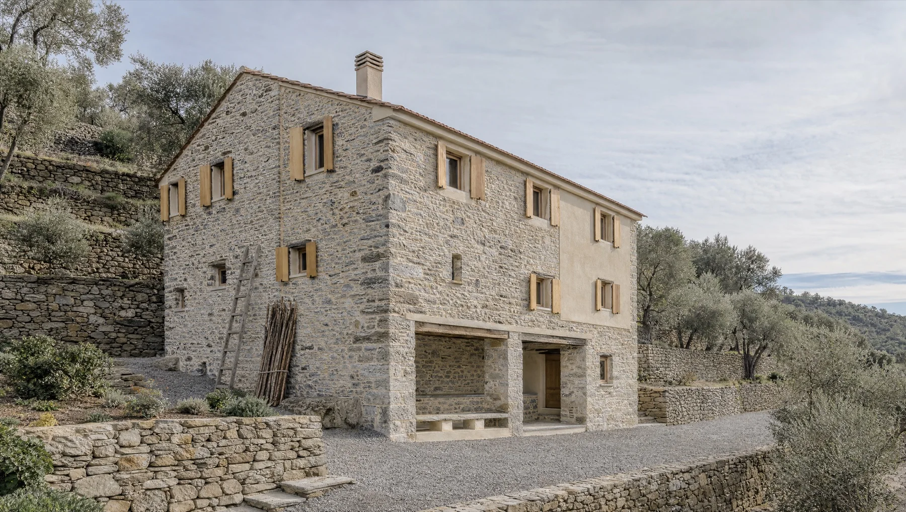 Casale in pietra a vista su tre piani, restaurato, con scuri di legno chiaro e portico al piano terra, su fasce di ulivi