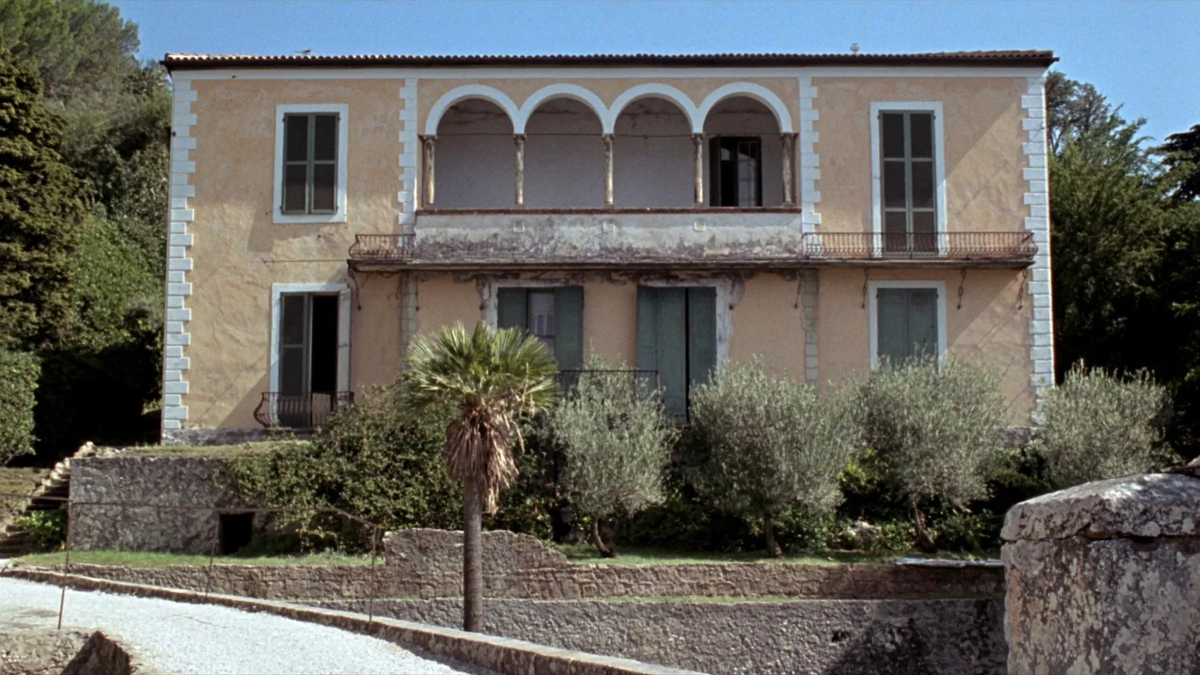 Facciata simmetrica di una villa d'epoca color ocra, con loggia a quattro archi al piano nobile, intonaco scrostato e giardino a terrazze davanti