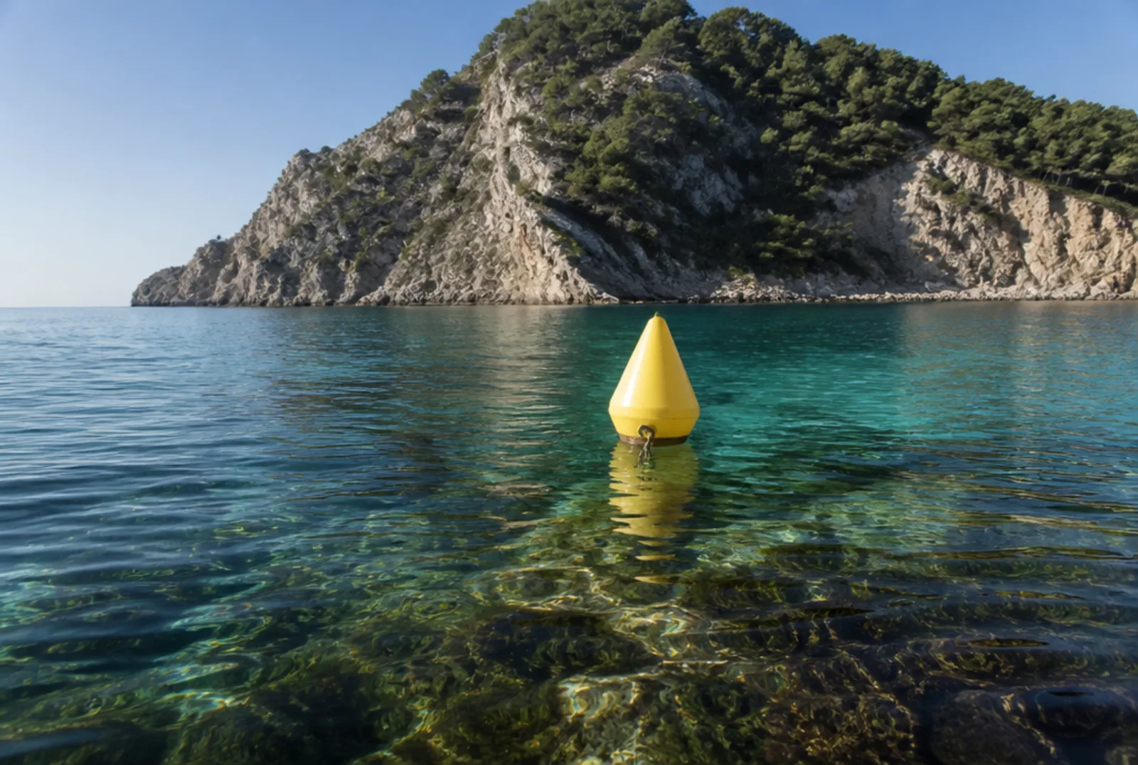 Una boa gialla di delimitazione su acqua trasparente, davanti al promontorio.