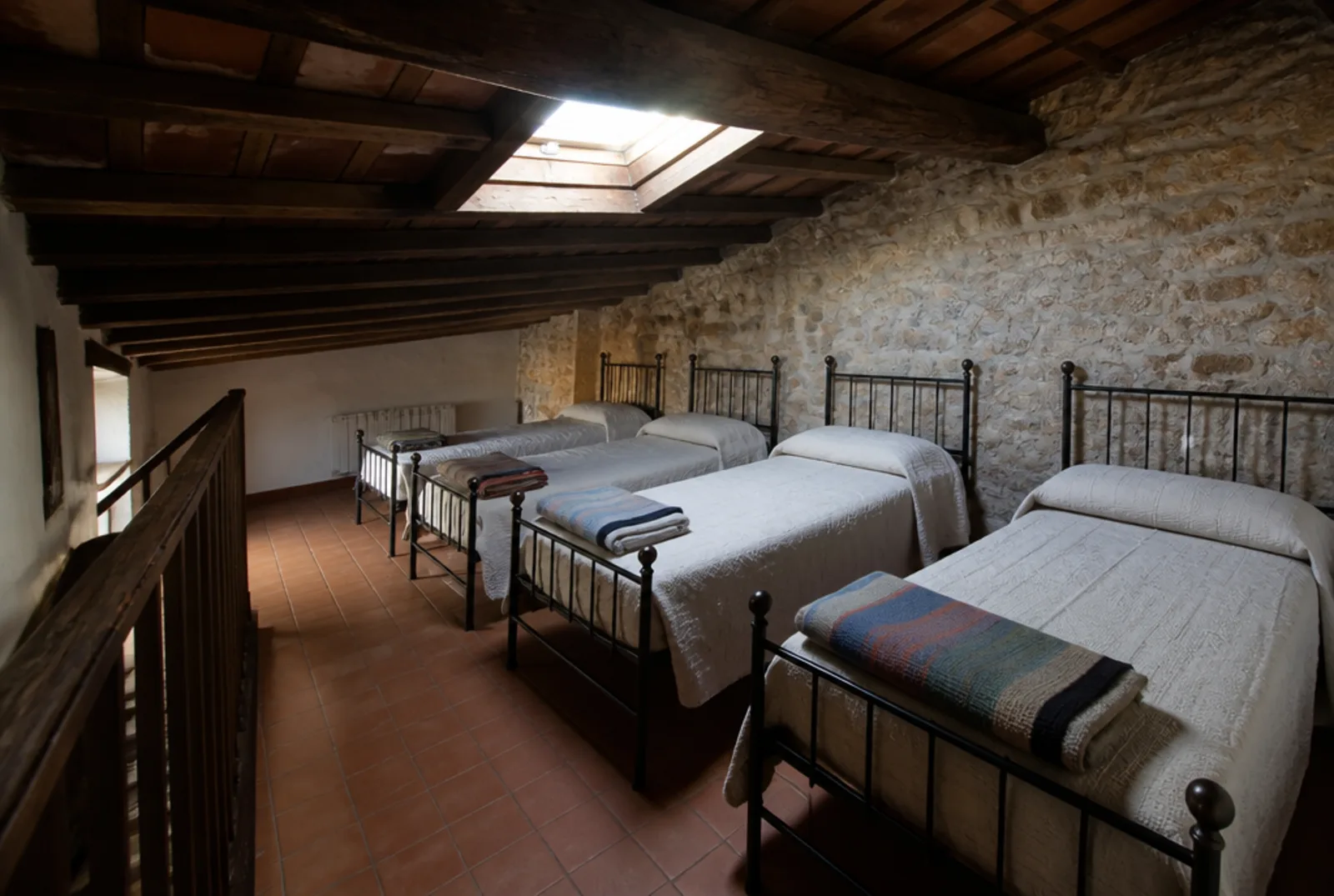 La camerata del sottotetto: quattro letti in ferro allineati sotto lo spiovente, pavimento in cotto e un lucernario aperto nel tetto