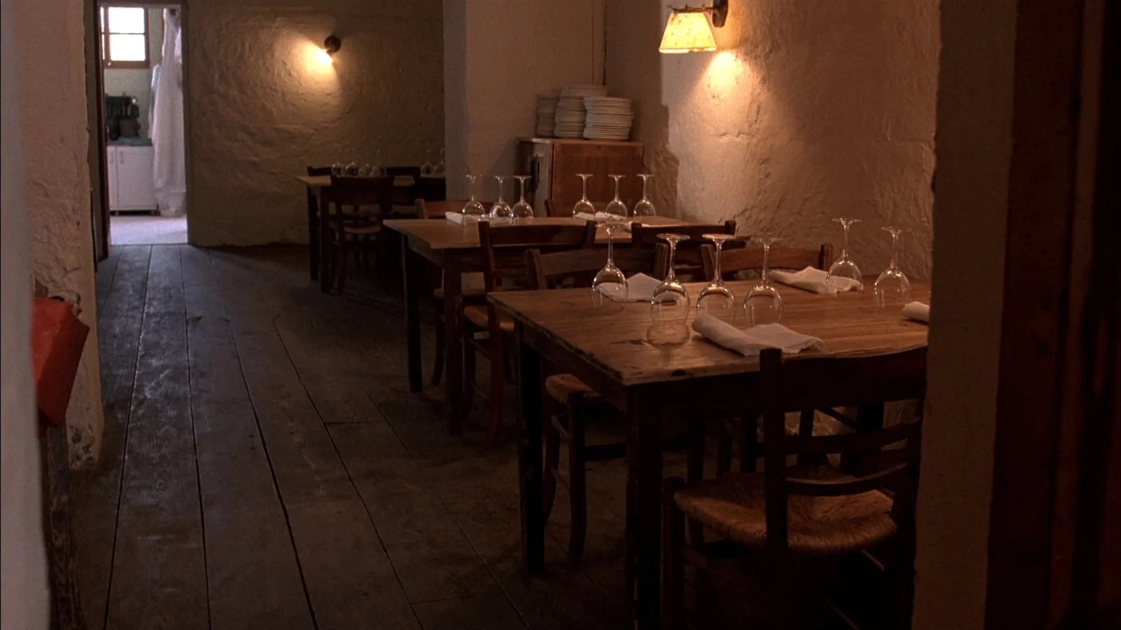 La sala della trattoria apparecchiata, muri a calce e tavoli di legno