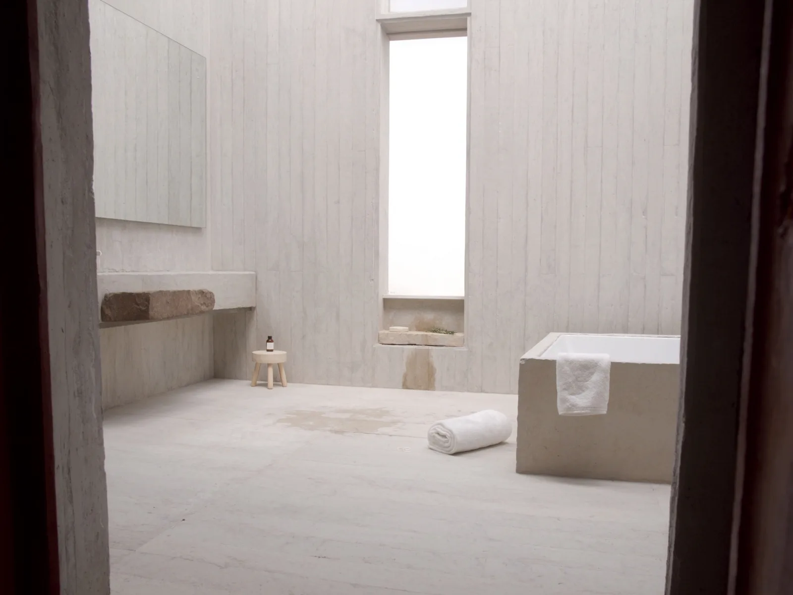 Bagno in calce grezza con vasca incassata in un blocco di pietra, mensola scavata nel muro e una feritoia verticale di luce